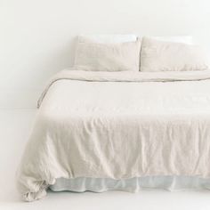 a white bed with two pillows on top of it and a blanket over the headboard