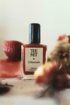 a bottle of nail polish sitting on top of a table next to flowers and fruit