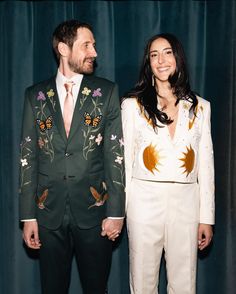 a man and woman standing next to each other in front of a blue curtain holding hands