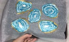 a person is painting some blue and gold cookies on a sheet of gray paper with white icing