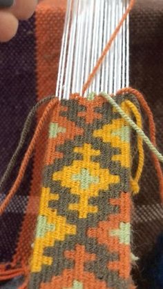 someone is weaving something on an orange and gray blanket