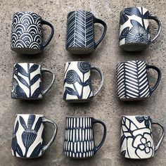 nine coffee mugs with designs on them are lined up against a concrete wall, one is blue and the other is white