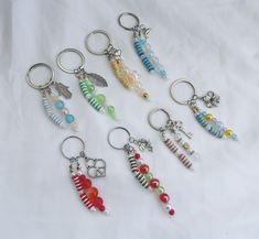 six different key chains with beads and charms attached to them on a white sheeted surface