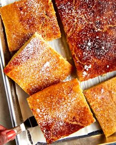 several square pieces of cake sitting on top of a pan covered in powdered sugar