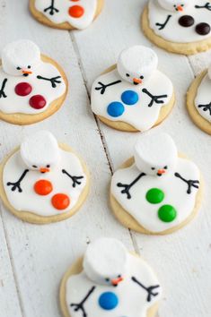 snowman cookies decorated with icing and colored candies on a white wooden surface