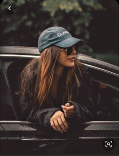 a woman in sunglasses and a hat leaning out the window of a car