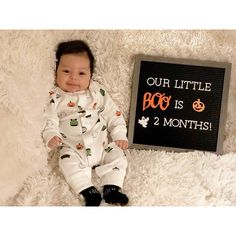 a baby laying next to a sign that says, our little boo is 2 months