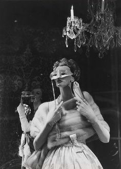 a woman with blindfolded eyes standing in front of a chandelier holding a mirror