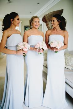 three bridesmaids standing in front of a couch holding bouquets and smiling at each other