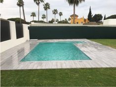 an empty pool surrounded by palm trees in a backyard with green grass and white walls