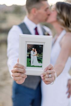 a bride and groom kissing in front of a white frame with an image on it