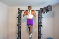 a woman in purple shorts is doing pull ups on a gym equipment rack with two dumbbells