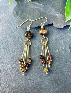 Make a statement with our Tiger's eye earrings! These eye-catching dangle earrings showcase natural tigerseye gemstones hanging beautifully from a golden hoop, giving you a unique and stylish vibe. Perfect for casual outings or special events, these earrings bring a natural charm to any outfit. EARRING FEATURES Total Length: Approximately 2.5 inches Gemstone: Tigerseye 4mm & 8mm  Metal: Gold Tone ♥ All orders come beautifully hand-packaged with care, making it the perfect gift for yourself or someone special. ♥ Each piece is handmade with love in my home studio in Rockaway, NJ. Fringe Beaded Earrings, Boho Jewelry Diy, Lampwork Bead Jewelry, Tiger Eye Jewelry, Gold Fringe, Jewelry Making Earrings, Earrings Inspiration, Crafts Jewelry, Earrings Dainty