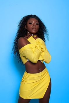 a woman in a yellow dress posing for the camera with her arms folded over her chest