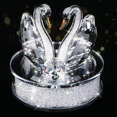 two crystal swans sitting on top of each other in a glass bowl with sparkles