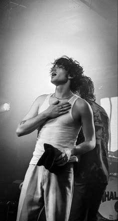 a black and white photo of a man with long hair standing in front of a microphone