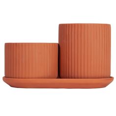 two clay cups and saucer set on a plate with an orange rim, one in the shape of a ribbed