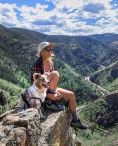 a woman sitting on top of a cliff next to a dog with mountains in the background