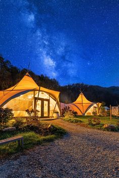 a couple of tents sitting on top of a lush green field under a night sky