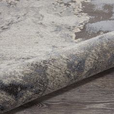 an area rug on the floor with wood floors and grey carpeting in the background