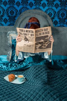 a woman reading a newspaper while sitting on a bed with pastries in front of her