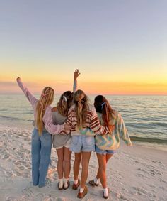 four girls standing on the beach with their arms in the air