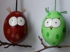 two green and red birds sitting on top of branches next to each other in front of a white wall