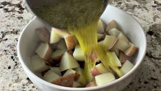 a bowl filled with potatoes being drizzled with dressing