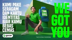 a man sitting on the ground in front of a green and blue advertisement with words