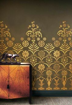 an ornate wallpaper design in gold on a brown background with a wooden cabinet and sideboard