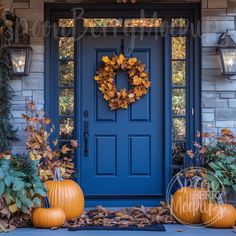 a blue front door with two pumpkins on the steps and an autumn wreath hanging over it