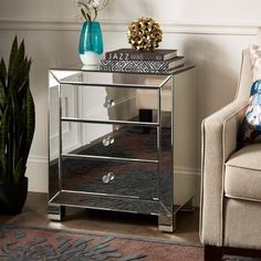 a mirrored side table with three drawers and a blue vase on top, next to a chair