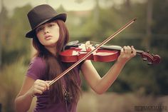 a young woman holding a violin in her right hand and wearing a hat on top of her head