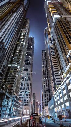 tall buildings are lit up at night in the middle of a city with cars driving down the street