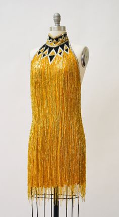 "80s Bob Mackie Super Chic Vintage Gold beaded and sequin dress features: * Silk chiffon body fully embellished with gold glass beads and stunning strands of beaded fringe * Beaded/sequined geometric pattern around neckline * Stunning t-strap back zip closure * Scalloped hemline * Fully lined with back zip closure * Great Vintage condition By Bob Mackie Boutique Size 6, fits like a small 100% silk Length from High point shoulder 33\" Bust 33\" Waist 30\" Hip 39\" All measurements are given in fu Summer Embellished Flapper Dress For Costume Party, Embellished Flapper Dress For Summer Costume Party, Embellished Flapper Dress For Party Season, Summer Party Embellished Flapper Dress, Summer Evening Beaded Sequin Dress, Sequin Flapper Dress For Gala And Party Season, Beaded Sequin Dress For Summer Parties, Gatsby Style Beaded Flapper Dress For Party, Gatsby Style Beaded Fringe Party Dress