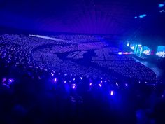 a large group of people sitting in front of a stage with purple lights on it