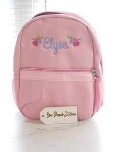 a pink backpack sitting on top of a white counter next to a window with the name elye written on it