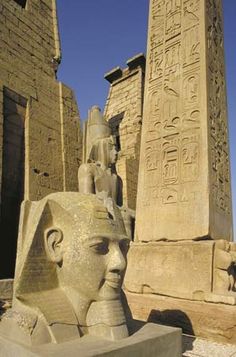 an ancient egyptian statue in front of two large obelisk heads with writing on them