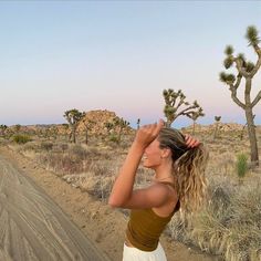 a woman standing in the middle of a dirt road next to a desert landscape with cacti