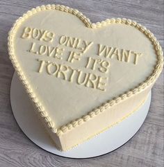 a white heart shaped cake with writing on the top and bottom that says boys only want love if it's torture