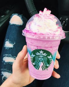 a person holding up a pink drink with whipped cream and sprinkles on it