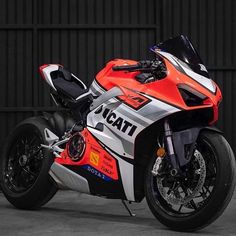 a red and white motorcycle parked in front of a black garage door with the words ducati on it