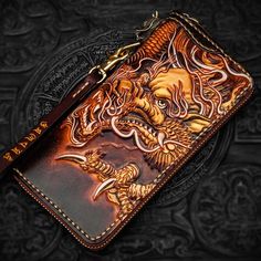 a brown leather wallet with an intricate dragon design on the front and side, sitting on top of a black background