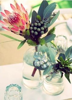 two vases filled with flowers and greenery on a white tablecloth covered table