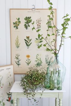 a white table topped with vases filled with flowers and greenery next to a poster