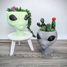 an alien head planter with succulents in it next to a white chair