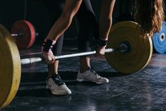 two women are doing squats with barbells in a gym together, one is holding the other's leg