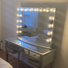 a vanity with lights on it and a bed in the background