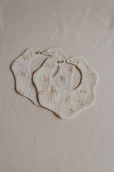 three bibs laying on top of a white cloth covered tablecloth with tiny flowers