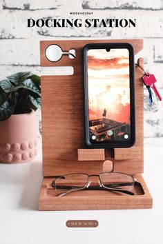 a wooden docking station with glasses, keys and cell phone on it next to a potted plant